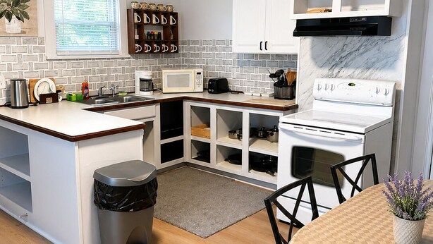 Een moderne keuken met witte kasten, een centraal eiland, een magnetron, een fornuis en een eethoek met een tafel en stoelen.