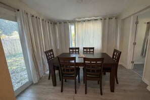 Ein Essbereich mit Tisch und Stühlen, einem Fenster mit Vorhängen und Blick ins Freie.