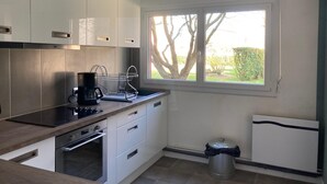 Una cocina moderna con armarios blancos, horno empotrado, cafetera y ventana con vista a árboles.