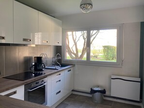 A modern kitchen with white cabinets, a built-in oven, a coffee maker, and a window with a view of trees. - Quiet Designer Apartment in Fecamp (Fecamp)