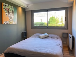 A bedroom with a bed, a window, a painting, and a radiator. - Quiet Designer Apartment in Fecamp (Fecamp)