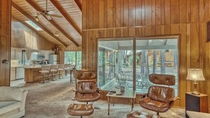 A spacious living area with leather chairs, a coffee table, and a large sliding glass door leading to an outdoor deck. - Pinetop Sinatra Getaway (Pinetop Country Club)