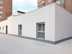 A modern building with a flat facade, large windows with metal bars, and a paved ground.