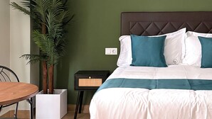 Ein Schlafzimmer mit Bett, Nachttisch, Stuhl, Tisch und einer Zimmerpflanze.