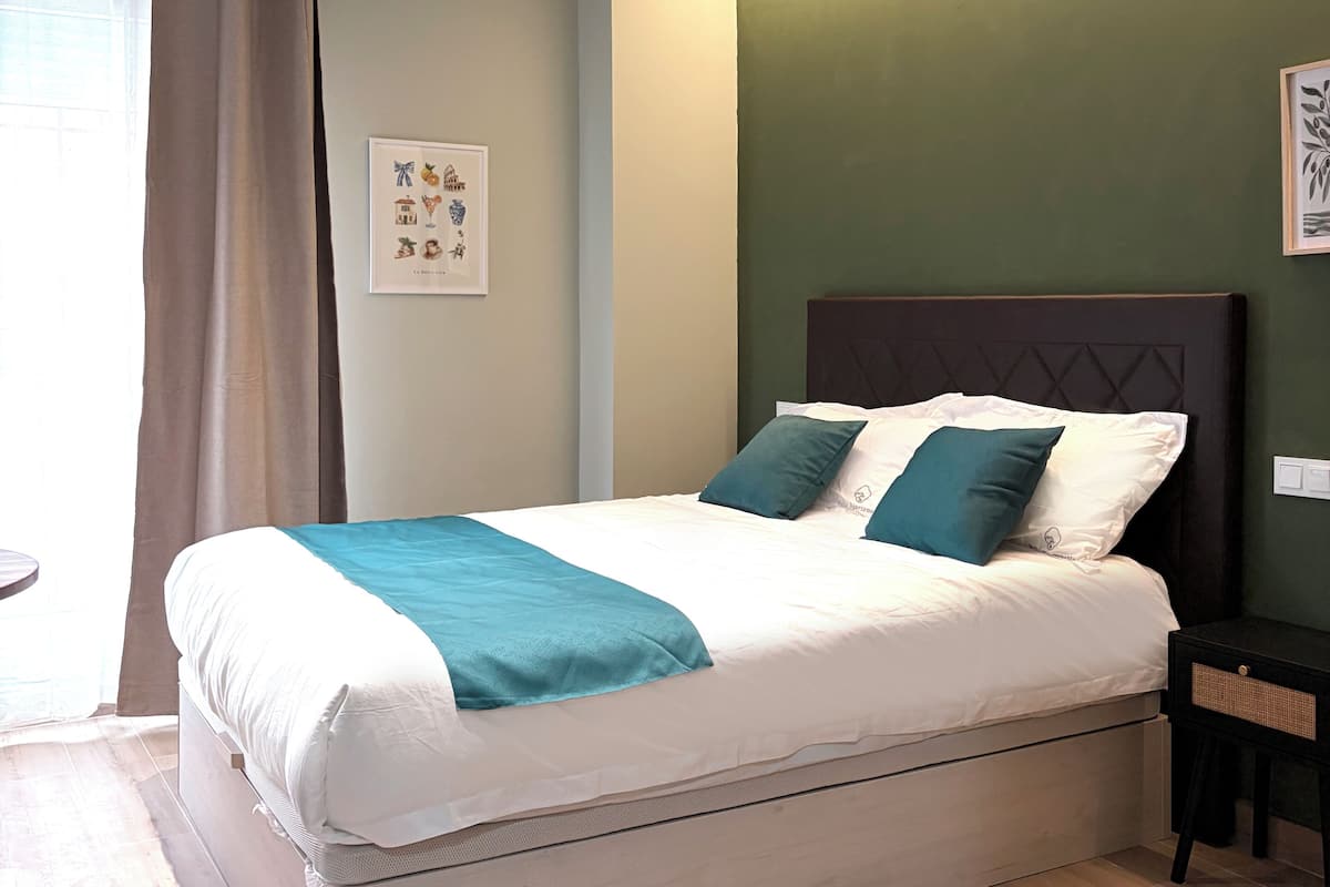 A neatly made bed with a white and teal bedspread, a dark headboard, and a green wall with a framed picture.