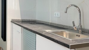 Eine moderne Küche mit Spüle aus Edelstahl, einer Arbeitsplatte aus Granit und weiß gefliesten Wänden.