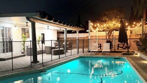 A swimming pool with a pergola and outdoor seating area, surrounded by a fence and string lights. - Modern Oasis with Heated Private Pool in Anaheim (Anaheim)
