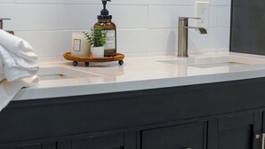 A bathroom with two round mirrors, a white sink, a black cabinet, and a small shelf with toiletries. - Modern Oasis with Heated Private Pool in Anaheim (Anaheim)