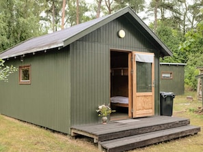 A small, green wooden cabin with a single open door, a small window, and a wooden deck. - 4 Star Holiday Home in Aakirkeby (Akirkeby)