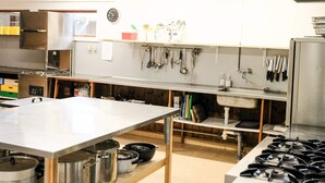 A kitchen with stainless steel appliances, a large table, and hanging utensils. - 4 Star Holiday Home in Aakirkeby (Akirkeby)