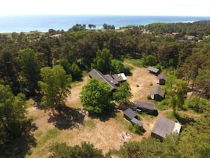 An aerial view of a residential area with multiple houses surrounded by dense forest, a clear view of the ocean, and a dirt path connecting the houses. - 4 Star Holiday Home in Aakirkeby (Akirkeby)