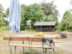 A wooden bench with a hat, a striped towel, and a yellow ball on a table in a natural setting with a cabin in the background. - 4 Star Holiday Home in Aakirkeby (Akirkeby)