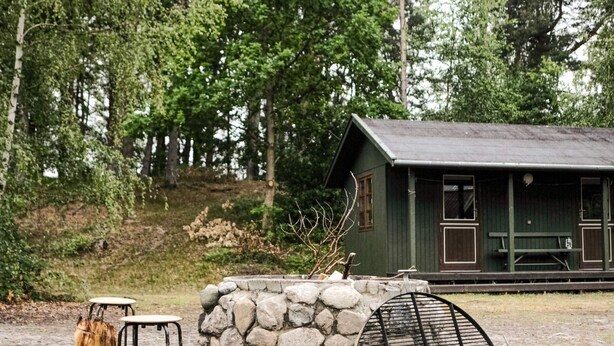 A rustic cabin with a stone wall, a wooden bench, and a metal grill. - 4 Star Holiday Home in Aakirkeby (Akirkeby)