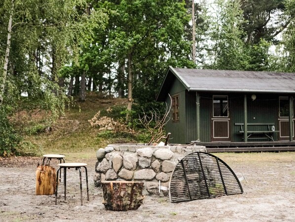 Eine rustikale Holzhütte mit Steinwand, Holzbank und Grillrost.
