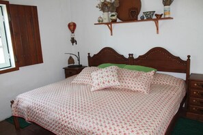 A bedroom with a wooden bed, green pillows, a bedside table with a lamp, and a shelf with decorative items.