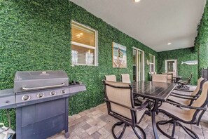 Eine Terrasse mit Grill, einem Esstisch und Stühlen sowie einer mit Grünpflanzen bewachsenen Wand.