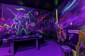 Ein Zimmer mit einer leuchtenden Wandmalerei zum Thema Weltraum, einer Spielkonsole und einem kleinen Hocker.