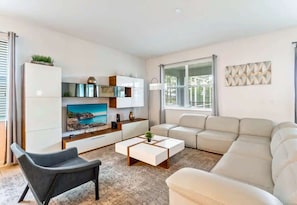 A modern living room with a sofa, a coffee table, a TV, and a cabinet. - Resort Lazy River! Themed 9BR! Close to Disney! (Four Corners)