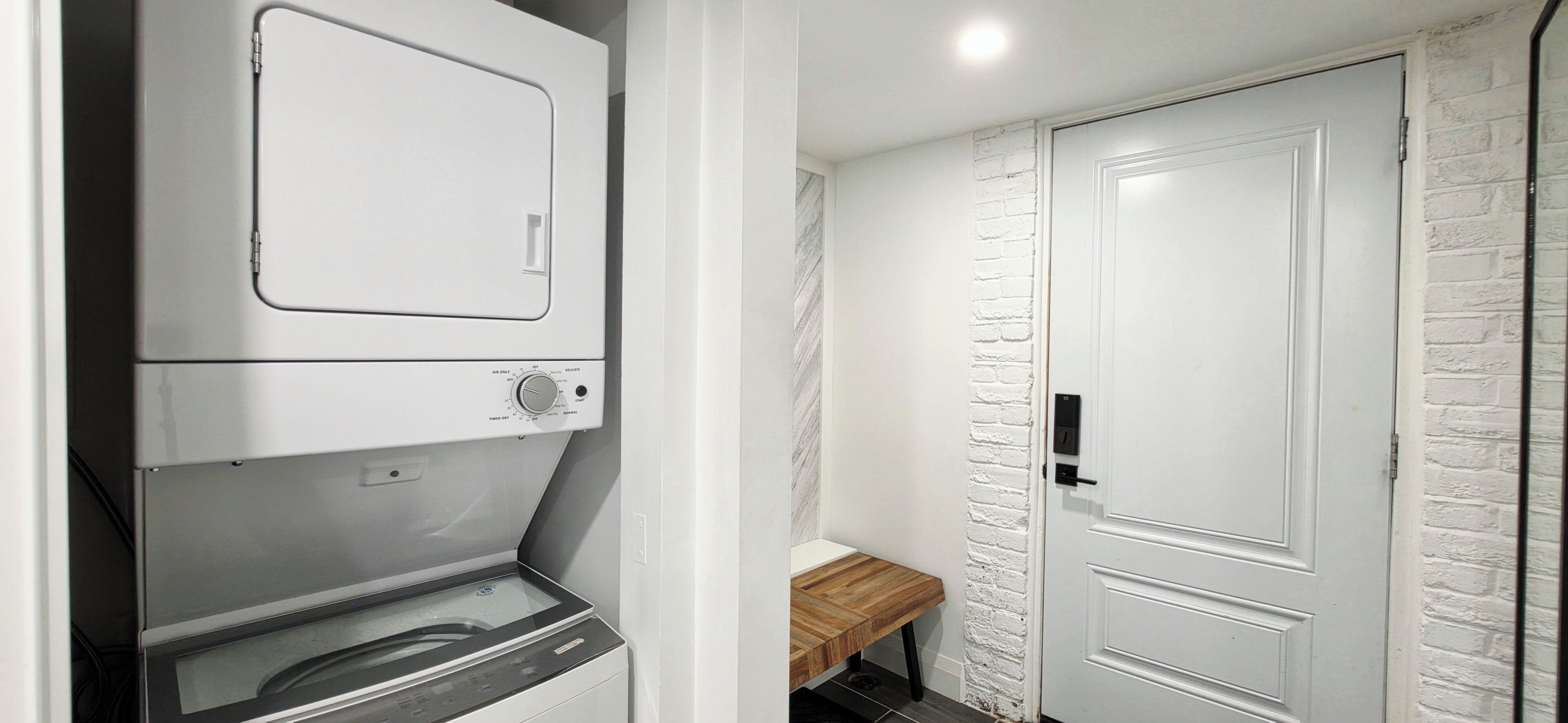 A laundry area with a washing machine and dryer, a white door, and a bench.