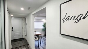 A hallway with a door, a framed sign with the word 'laugh,' and a dining area with a table and chairs.