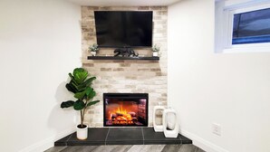 A modern living room with a fireplace, a flat-screen TV mounted above it, and a potted plant.