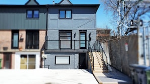 Une maison moderne à deux étages, dotée d’une façade en pierre, d’un garage dont la porte est visible et d’un escalier menant à l’entrée.