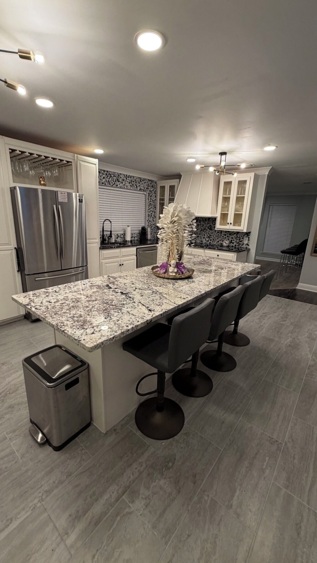 A modern kitchen with a granite island, stainless steel appliances, and a trash bin.