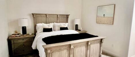 A bedroom with a bed, nightstands, a ceiling fan, a wall-mounted picture, and a carpeted floor.