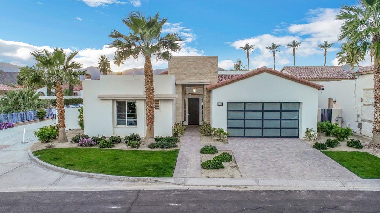 A modern two-story house with a garage, surrounded by well-maintained landscaping and palm trees.