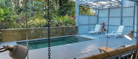 A covered outdoor area with a pool, lounge chairs, and a swing.