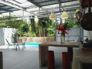 Um pátio externo com piscina, uma mesa com um vaso de flores e luminárias pendentes.