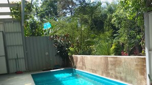 Une piscine rectangulaire bordée de béton, entourée d’un muret en béton et d’une clôture en bois.