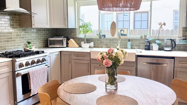Una cocina moderna con una mesa de comedor redonda, sillas de madera, una lámpara colgante y vistas al exterior a través de amplios ventanales.