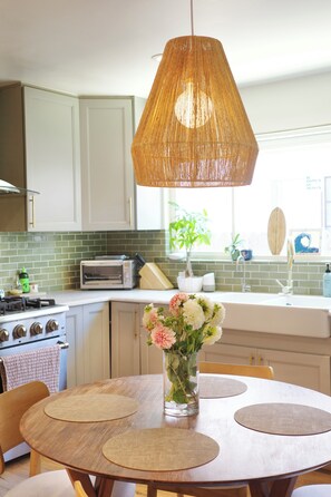 A kitchen with a round wooden table, a hanging light fixture, and a vase with flowers. - Spanish Oasis in Miracle Mile w/ Backyard (Los Angeles)