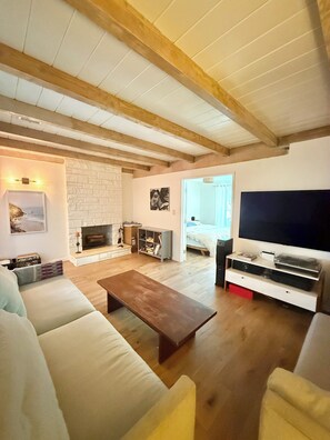 A living room with a fireplace, a sofa, a coffee table, a TV, and wooden beams on the ceiling. - Spanish Oasis in Miracle Mile w/ Backyard (Los Angeles)