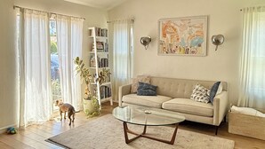 Una sala de estar con un sofá, una mesa de centro de vidrio, una estantería y un cuadro en la pared.
