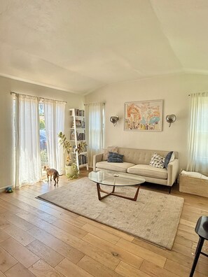 Ein Wohnzimmer mit einer Couch, einem Glastisch, einem Bücherregal und einem Gemälde an der Wand.