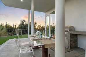 An outdoor patio with a glass table, white chairs, and a barbecue grill. - Valley Hills Estate with Water slide, 2 Pools, Sauna & Views (Los Angeles)