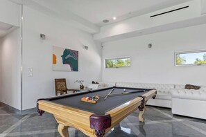 A modern living room with a pool table, a white sofa, and a painting on the wall. - Valley Hills Estate with Water slide, 2 Pools, Sauna & Views (Los Angeles)
