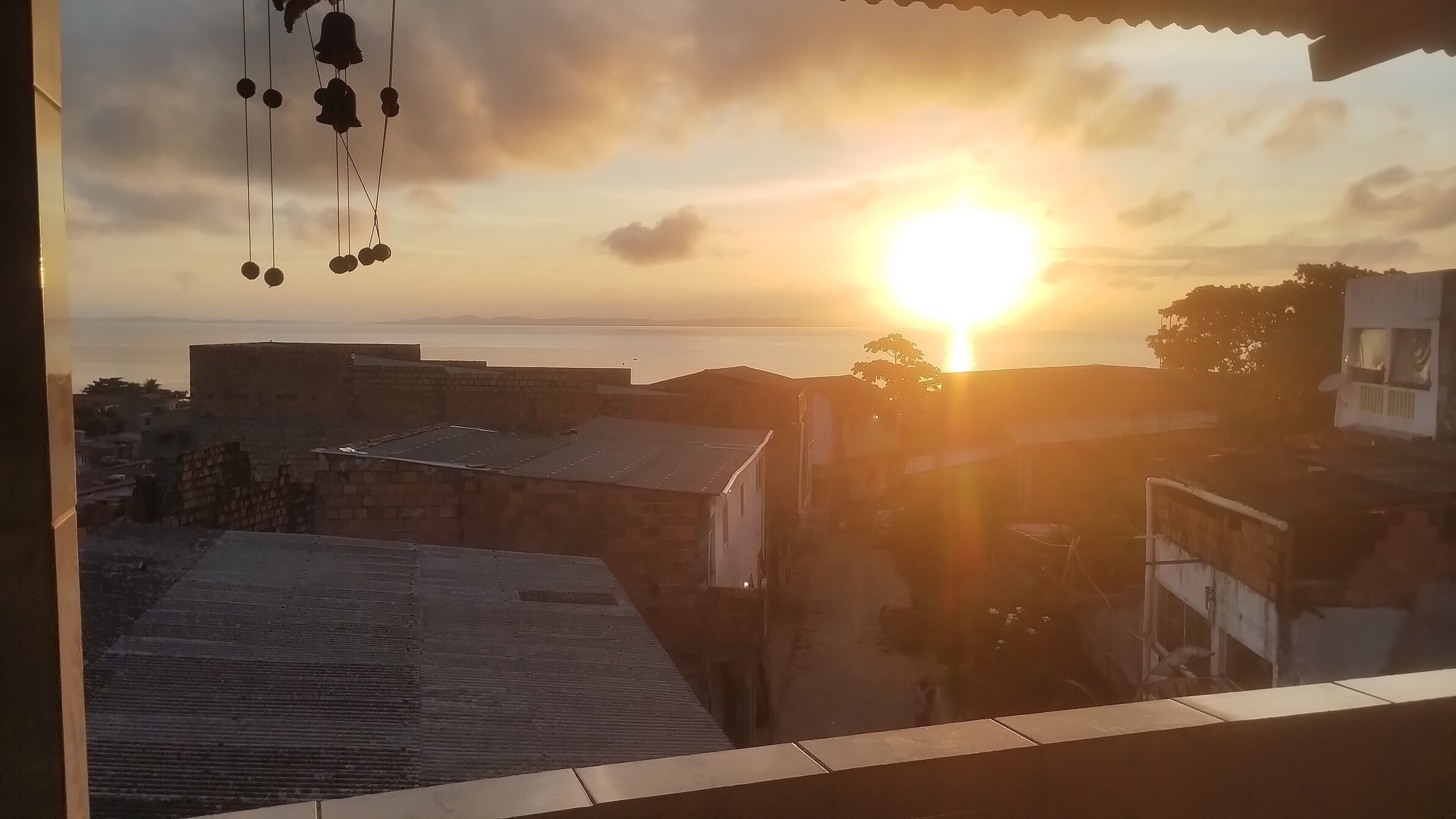 Vista do pôr do sol por uma janela com vista para um horizonte urbano, com edifícios e um corpo de água.