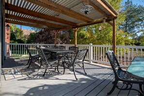 A covered patio with a table and chairs, a white fence, and a view of trees and a building in the background. - Charming 4-bedroom house in Fruit and Wine country  Palisade! Retired BnB (Palisade)