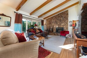 A living room with a stone wall, a fireplace, a red chair, and a wooden coffee table. - Charming 4-bedroom house in Fruit and Wine country  Palisade! Retired BnB (Palisade)