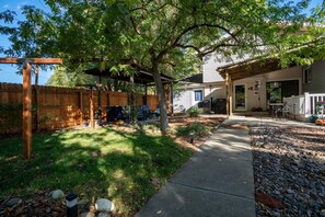 A backyard with a wooden fence, a covered patio area, and a house with a garage. - Charming 4-bedroom house in Fruit and Wine country  Palisade! Retired BnB (Palisade)