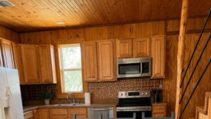 A wooden kitchen with a large table, cabinets, a microwave, and a stove. - The Farmhouse at the Starlight PK Ranch and Venue on Possum Kingdom Lake (Graham)