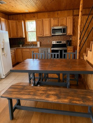 Una cocina de madera con una mesa grande, armarios, un microondas y una estufa.