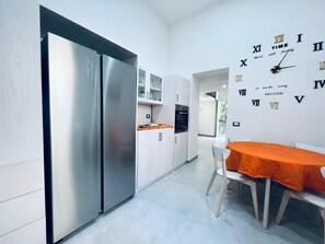 Eine moderne Küche mit einem Edelstahlkühlschrank, weißen Schränken und einem Essbereich mit einem orangefarben gedeckten Tisch.