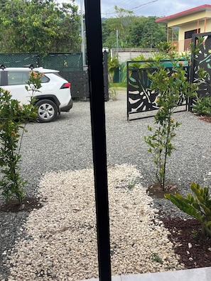 Ein unbefestigter Weg führt zu einem eingezäunten Eingang, in dessen Nähe ein weißes Auto geparkt ist.
