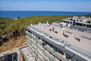 A modern building with multiple floors, large windows, and a rooftop terrace with seating. - OHANA 5 Mrzeżyno - Beachfront Apartment (Mrzeżyno)