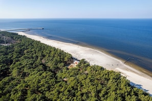 An aerial view of a beach with a pier extending into the sea, surrounded by dense forest. - OHANA 5 Mrzeżyno - Beachfront Apartment (Mrzeżyno)