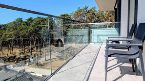 Ein Balkon mit Glasgeländer, einem Stuhl und Blick auf Bäume und ein Gebäude.
